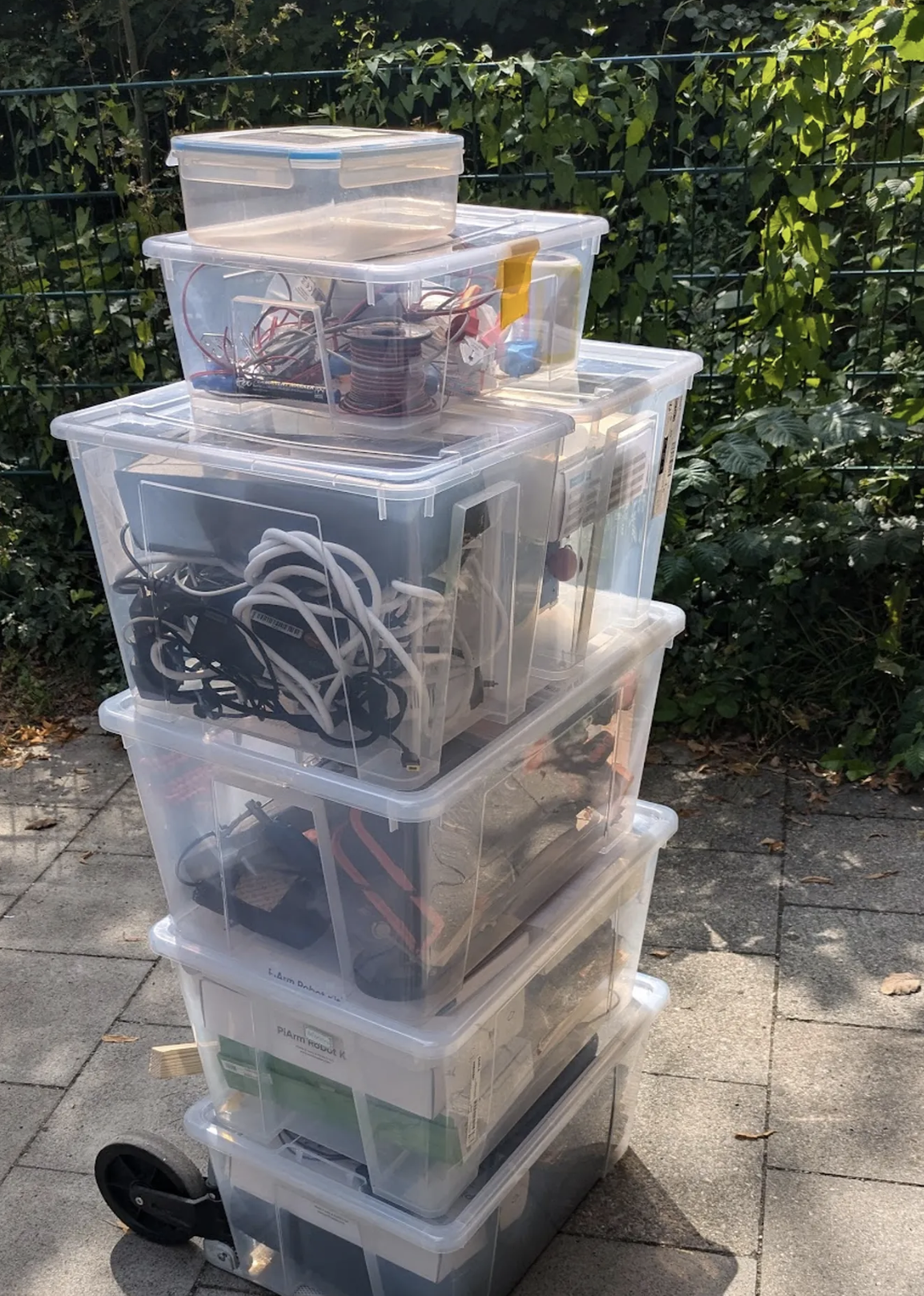 Mehrere gestapelte Plastikboxen mit Kabeln, Elektronikkomponenten und Materialien für den Unterricht.