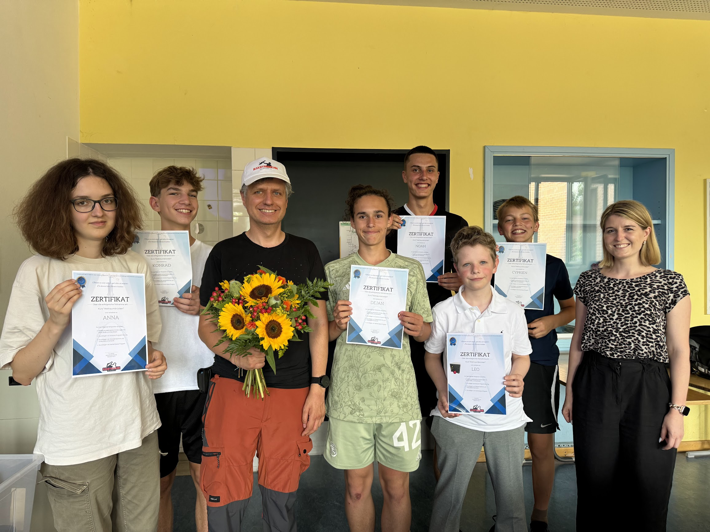 Gruppenfoto der Teilnehmer mit ihren Zertifikaten und dem Kursleiter, der einen Blumenstrauß hält.